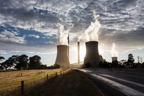 Zwei rauchende Schornsteine von einem Kohlekraftwerk im Sonnenuntergang. Das Bild symbolisiert das nahe Ende von fossilen Energieträgern und einem Umdenken.